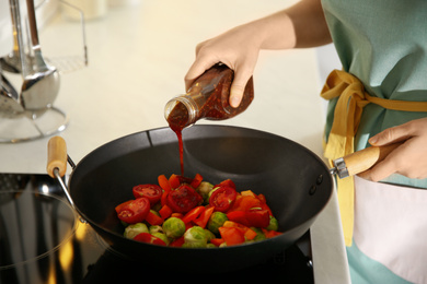 Photo of Young woman cooking on stove in kitchen, closeup