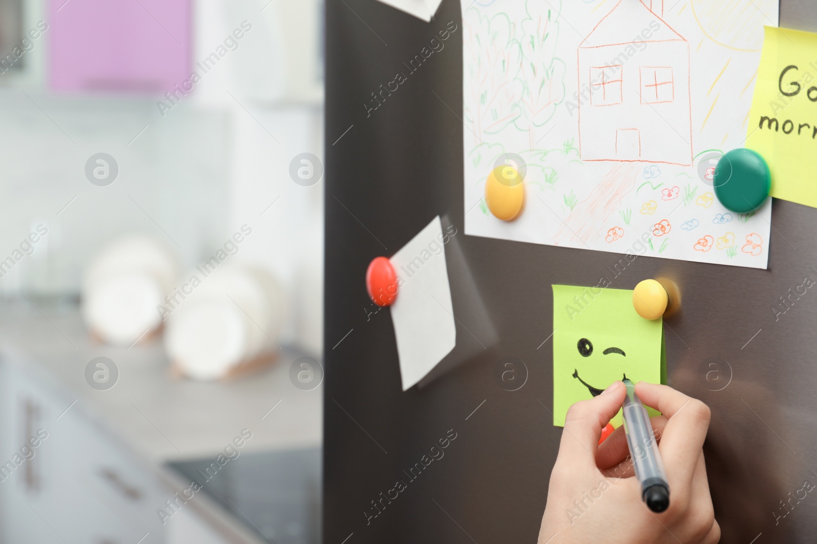 Photo of Woman drawing happy smile on note stuck to refrigerator door indoors, closeup