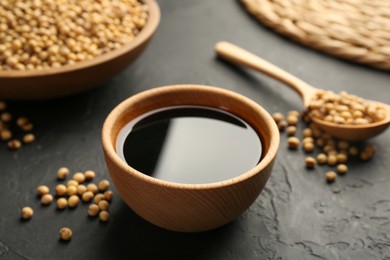 Tasty soy sauce in bowl and soybeans on black table, closeup