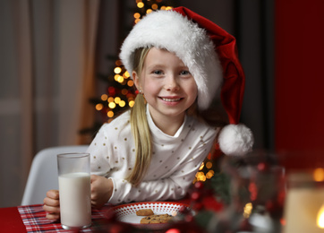 Photo of Cute little child with milk and cookies at table in dining room. Christmas time