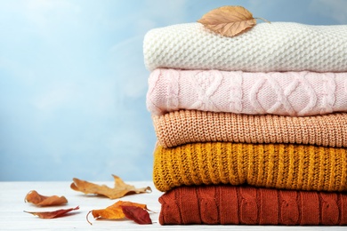 Photo of Stack of warm clothes and autumn leaves on white wooden table against light blue background