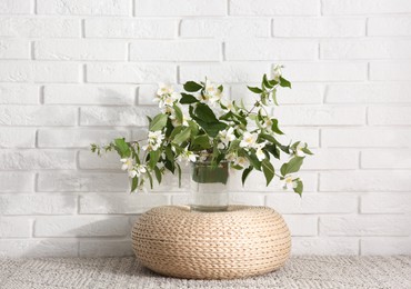 Photo of Bouquet of beautiful jasmine flowers in glass vase near white brick wall indoors