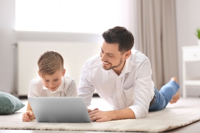 Photo of Little boy and his dad using laptop at home