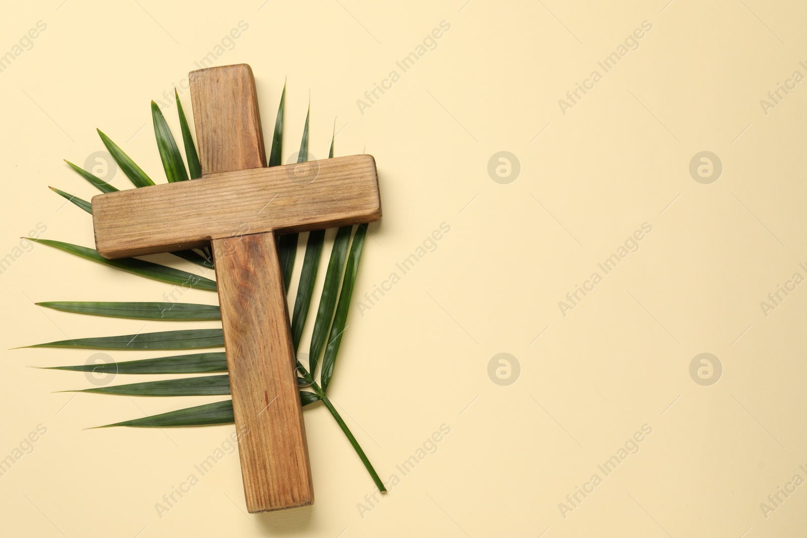 Photo of Wooden cross and palm leaf on beige background, top view with space for text. Easter attributes