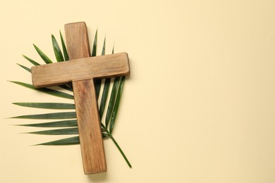 Wooden cross and palm leaf on beige background, top view with space for text. Easter attributes