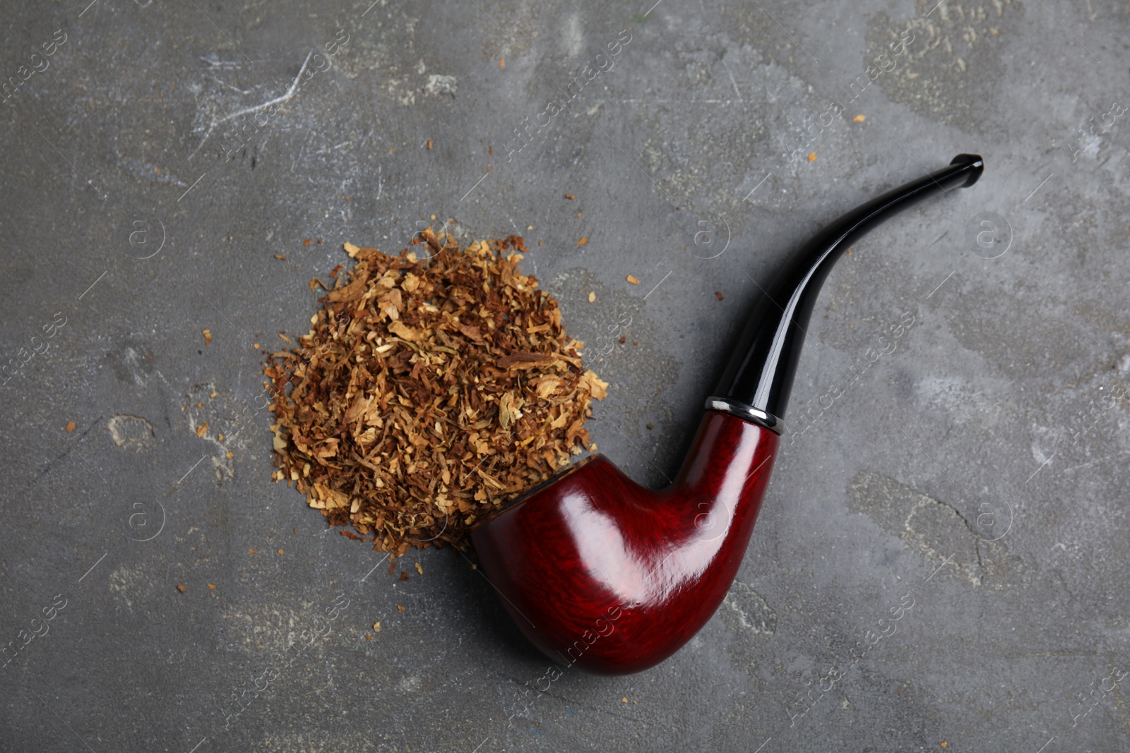 Photo of Pile of tobacco and smoking pipe on grey table, flat lay