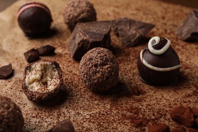 Photo of Different delicious chocolate truffles on parchment paper, closeup