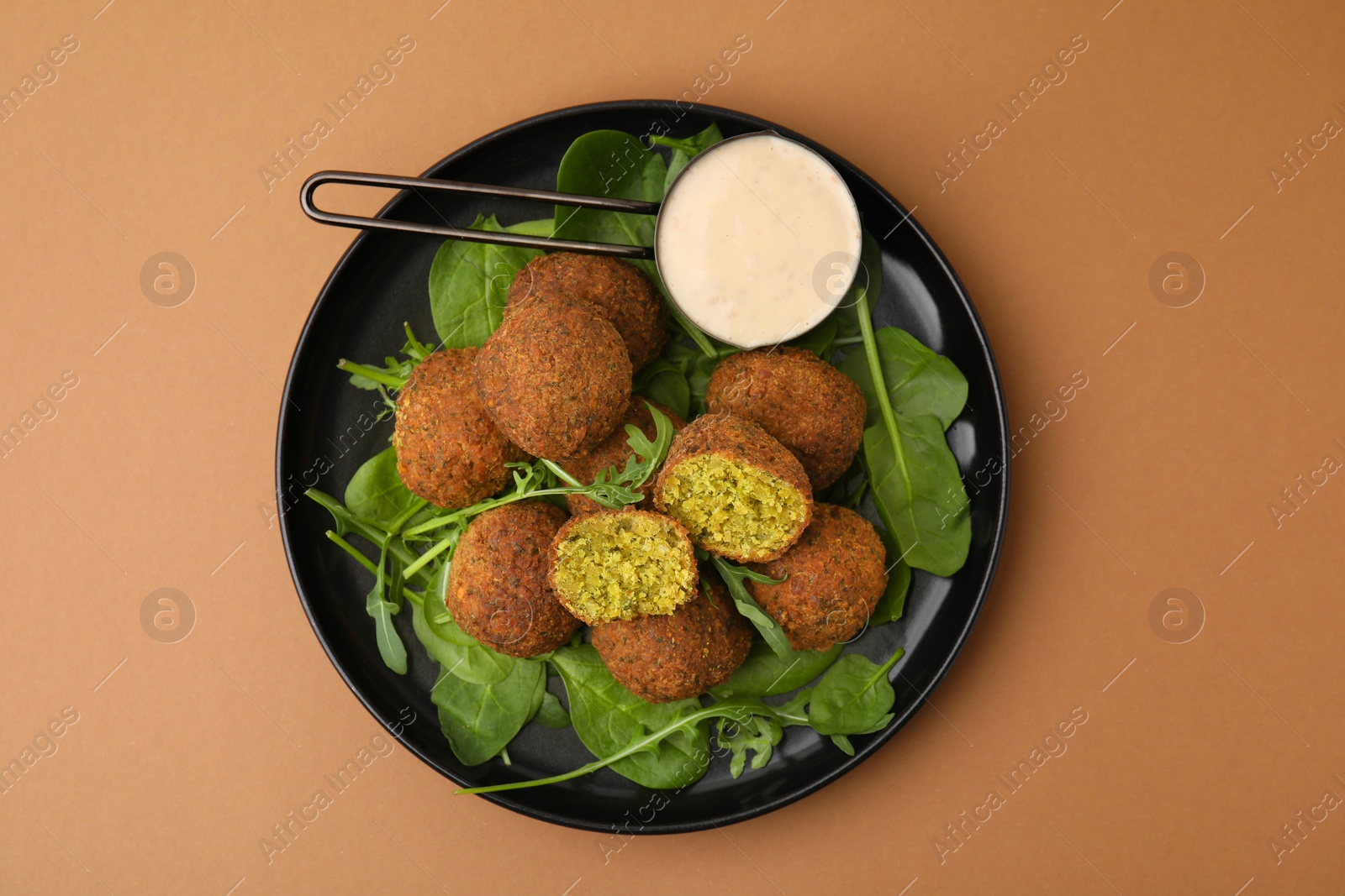 Photo of Delicious falafel balls, herbs and sauce on pale brown, top view