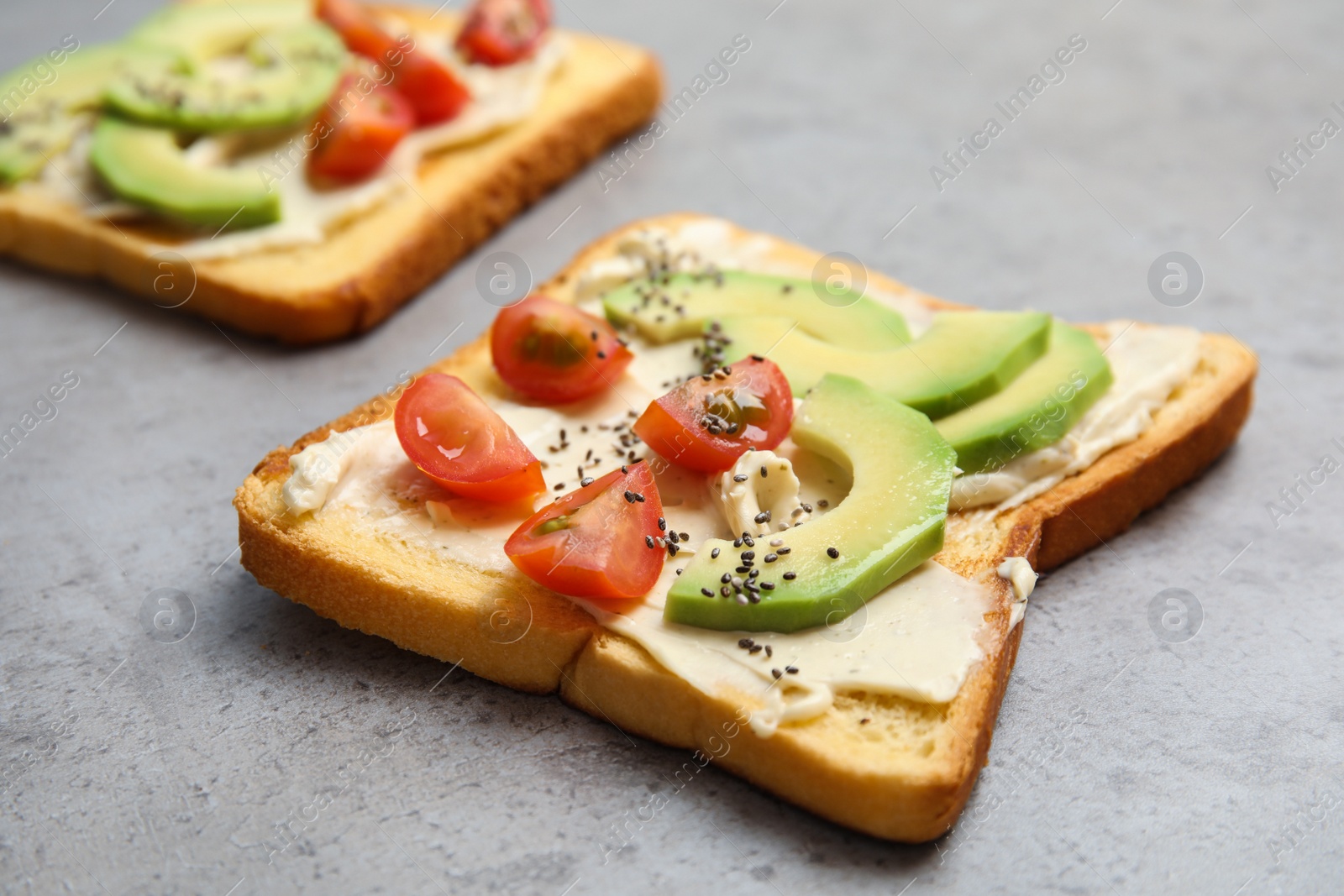 Photo of Tasty toast with avocado, cherry tomato and chia seeds on grey background
