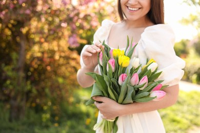 Young woman with bouquet of tulips in park on sunny day, closeup. Space for text