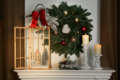 Photo of Beautiful festive lantern and candles on mantel near Christmas wreath