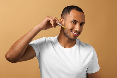Photo of Handsome man applying cosmetic serum onto face on light brown background