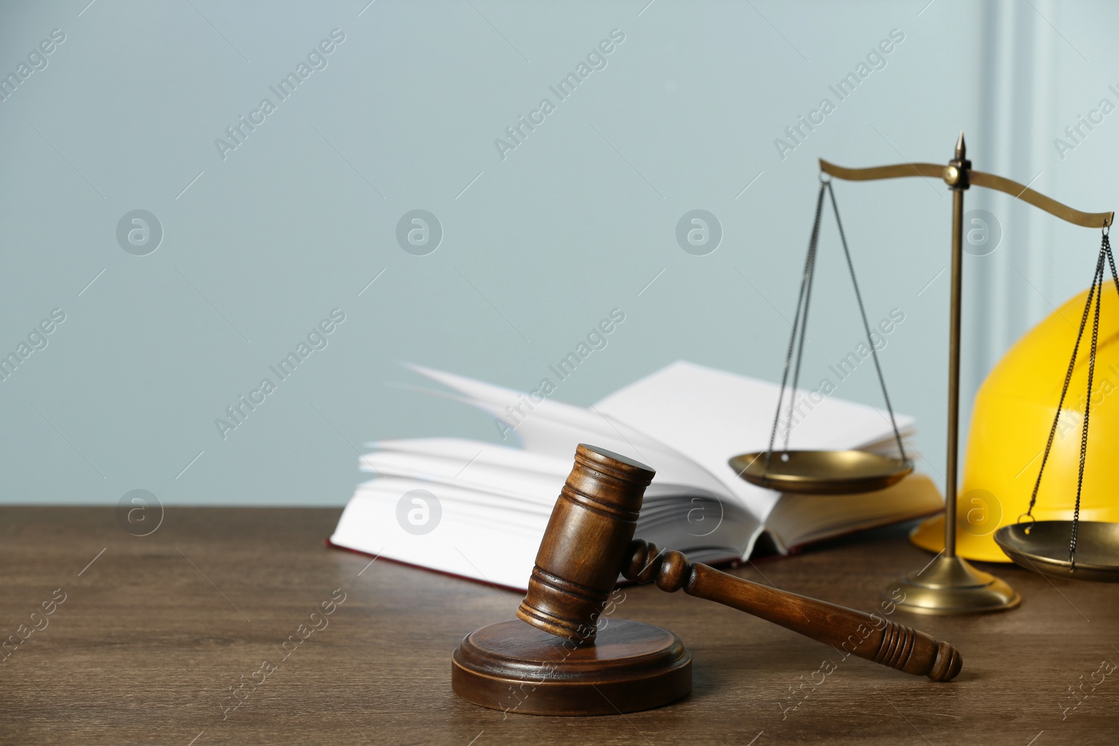Photo of Labour, construction and land law concepts. Judge gavel, scales of justice, open book with protective helmet on wooden table, space for text