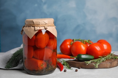 Photo of Jar with pickled tomatoes and vegetables on grey table against blue background