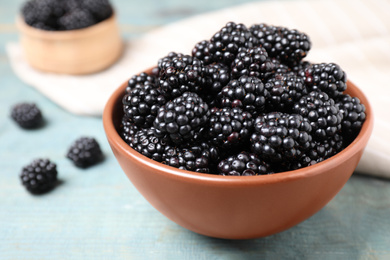 Photo of Fresh ripe blackberries in bowl on blue wooden table, closeup