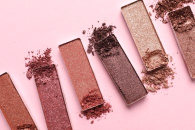 Photo of Different crushed eye shadows on pink background, flat lay. Professional makeup product