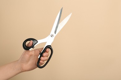 Photo of Woman holding tailor's scissors on beige background, closeup. Space for text