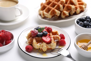Photo of Delicious Belgian waffles with fresh berries and honey served on white table