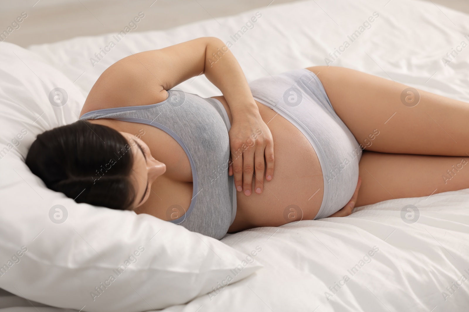 Photo of Beautiful pregnant woman in comfortable maternity underwear lying on bed