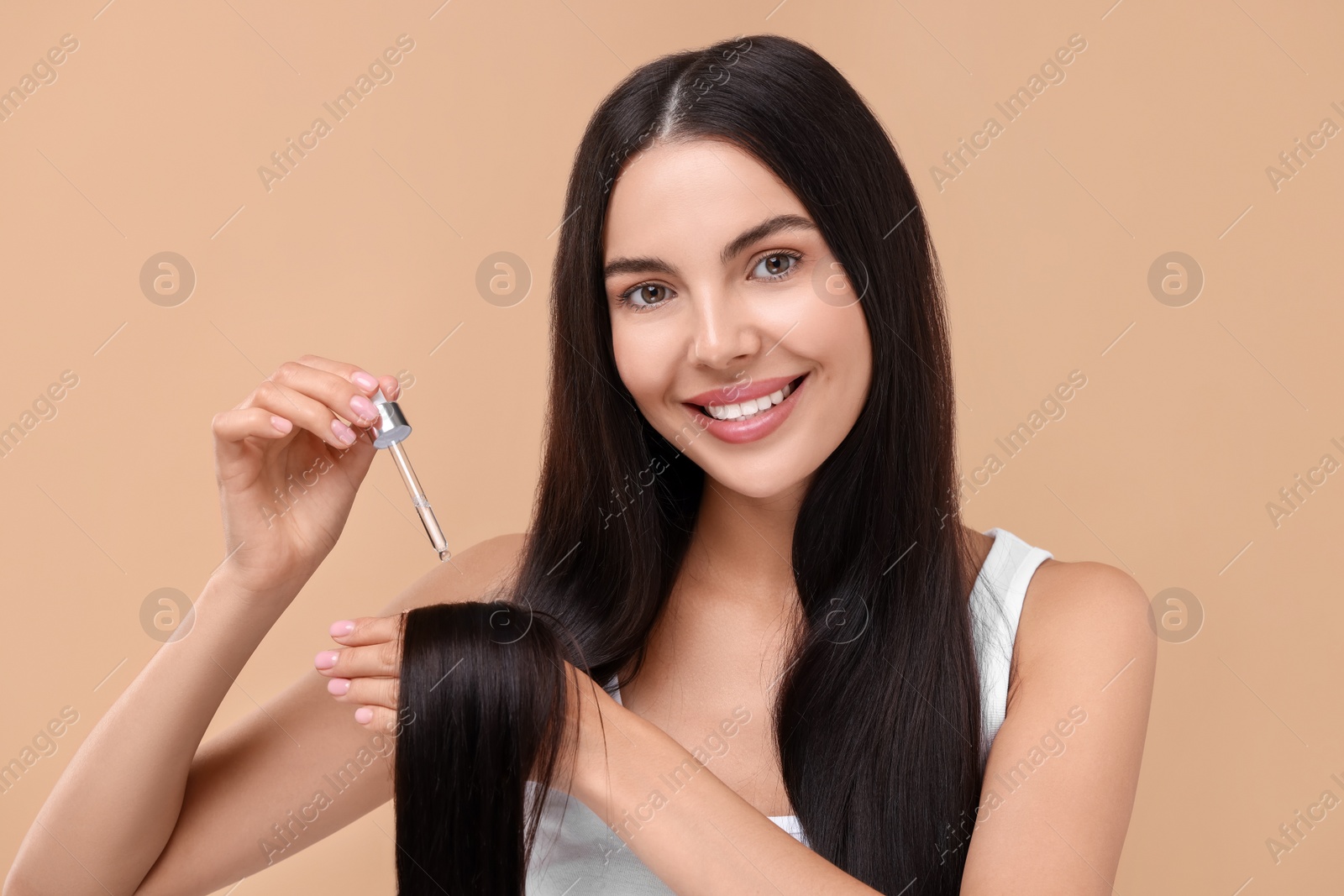 Photo of Beautiful woman applying hair serum on beige background. Cosmetic product