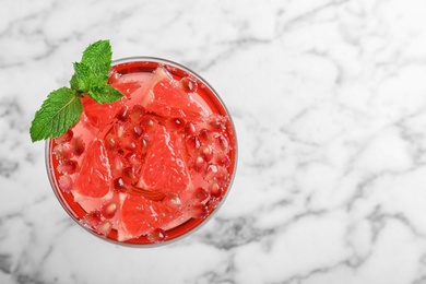 Photo of Glass of tasty refreshing cocktail with grapefruit and pomegranate on white marble background, top view. Space for text