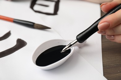 Calligraphy. Woman dipping brush into inkwell at table, closeup