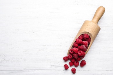 Scoop with delicious ripe raspberries on white wooden table, top view. Space for text