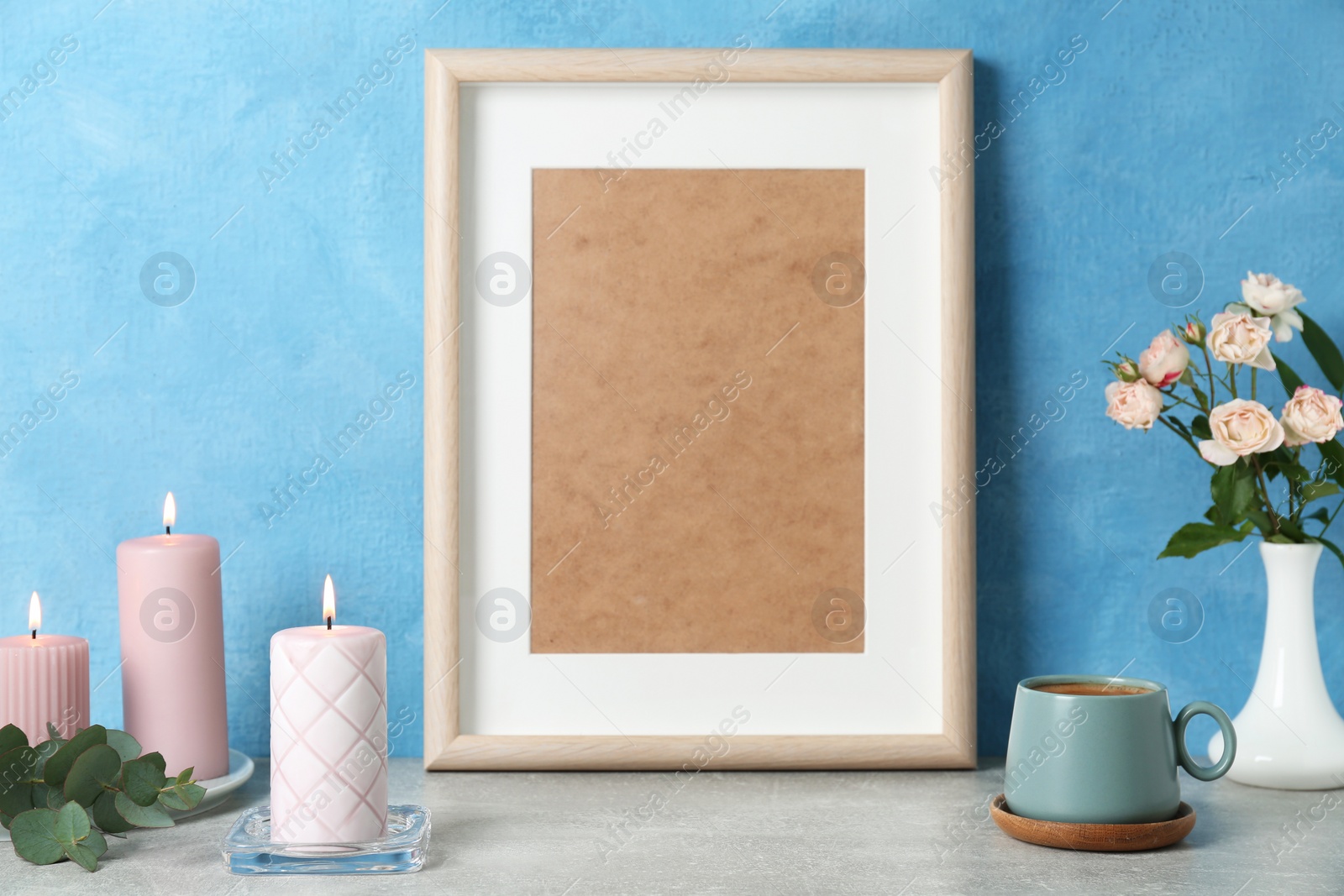 Photo of Scented candles, photo frame, flowers and cup on grey table near light blue wall