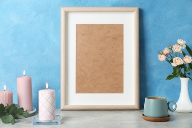 Photo of Scented candles, photo frame, flowers and cup on grey table near light blue wall