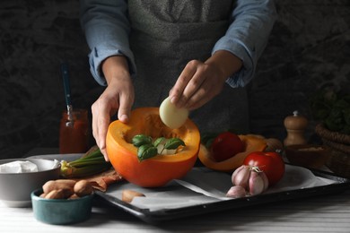 Photo of Woman stuffing pumpkin with vegetables at table, closeup