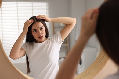 Photo of Emotional woman examining her hair and scalp near mirror in bathroom. Dandruff problem