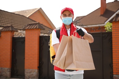 Photo of Courier in protective mask and gloves with order outdoors. Restaurant delivery service during coronavirus quarantine