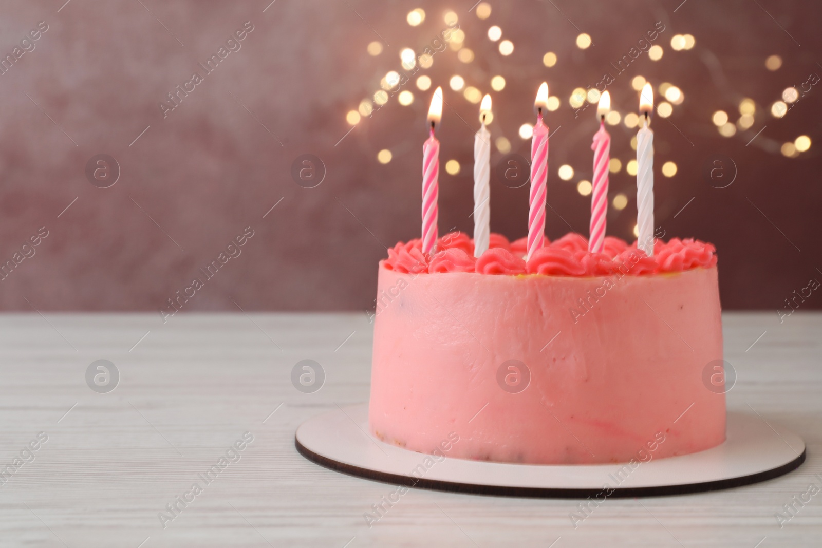 Photo of Cute bento cake with tasty cream and burning candles on white wooden table. Space for text