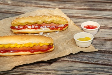 Photo of Fresh delicious hot dogs and sauces on wooden surface