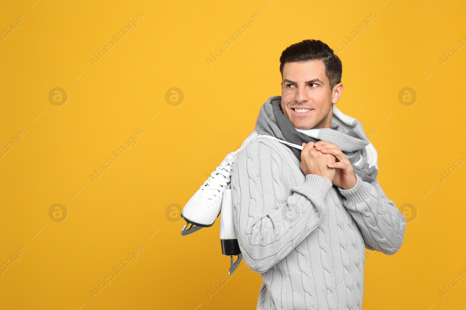 Photo of Happy man with ice skates on yellow background. Space for text