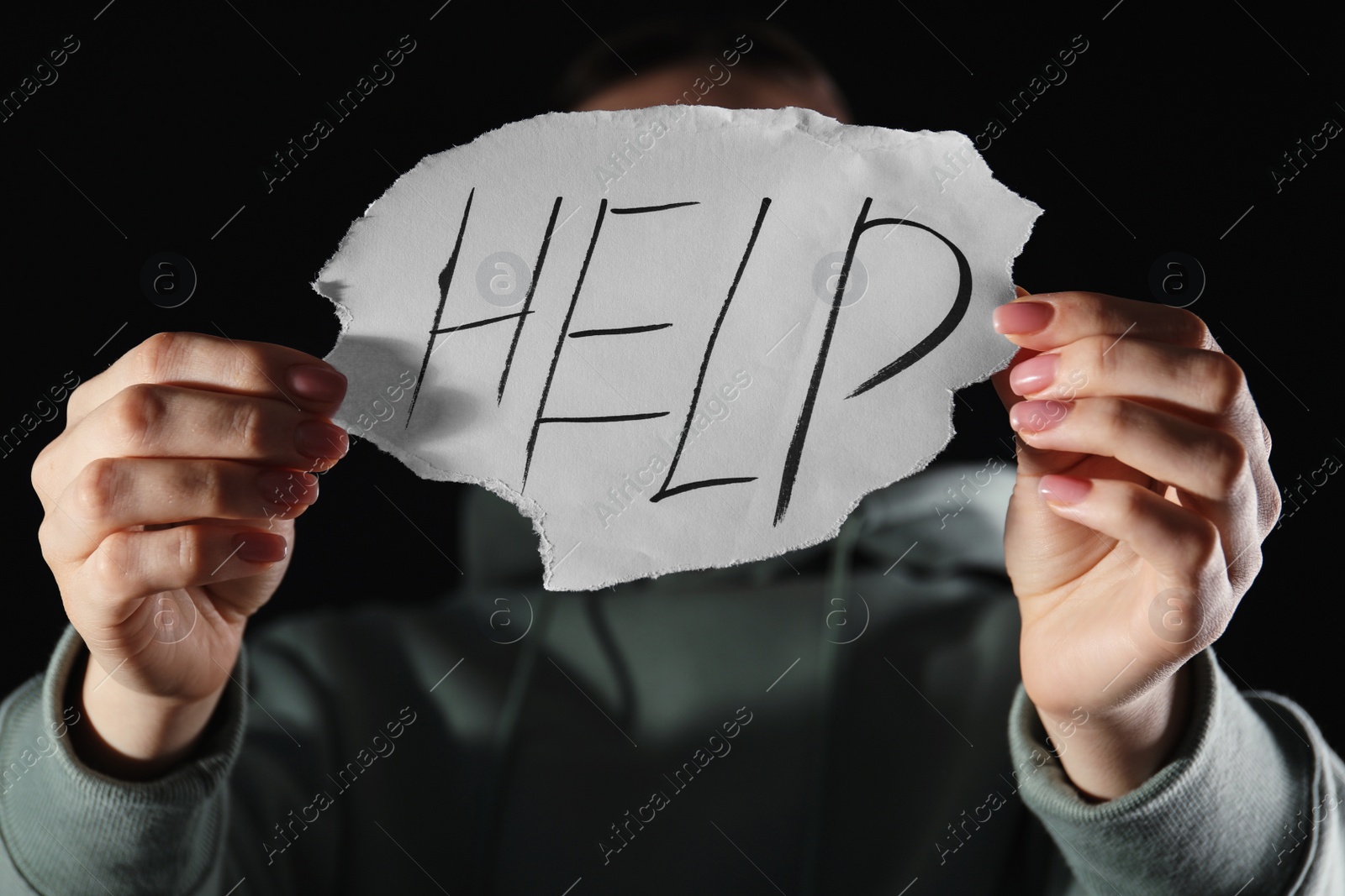 Photo of Woman holding piece of paper with word Help on black background, closeup. Domestic violence concept