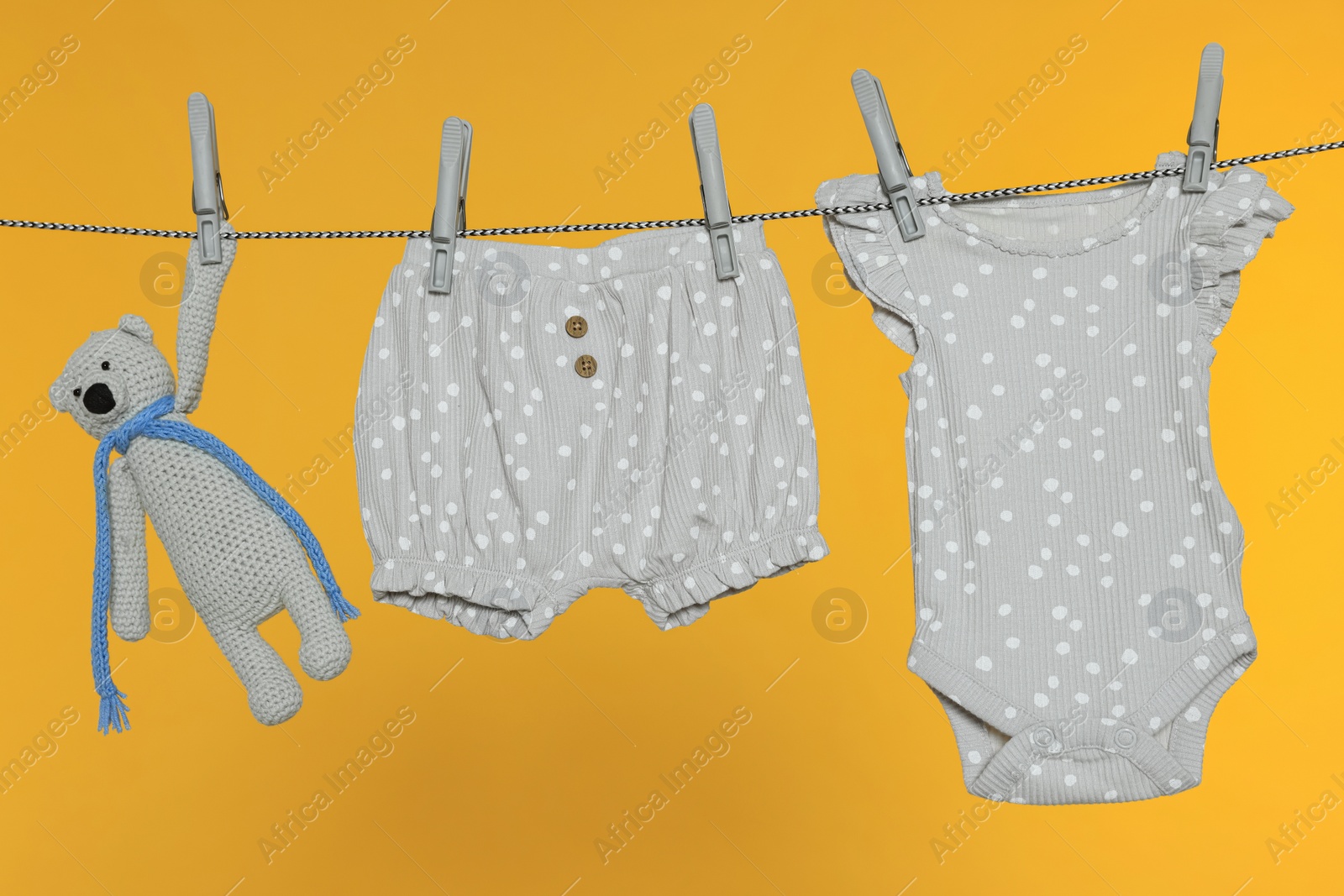 Photo of Baby clothes and bear toy drying on laundry line against orange background