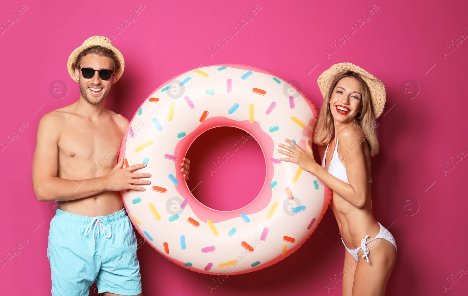 Photo of Happy young couple in beachwear with inflatable ring on color background