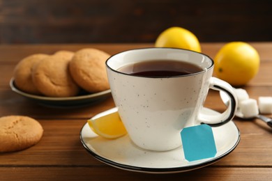 Photo of Tea bag in ceramic cup of hot water and lemon on wooden table