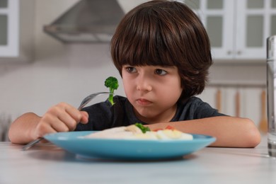 Photo of Cute little boy refusing to eat dinner in kitchen