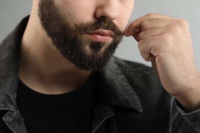 Young man touching mustache on grey background, closeup