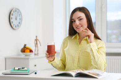 Photo of Beautiful young woman with delicious smoothie at table indoors