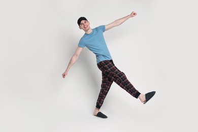 Happy man in pyjama and sleep mask on light grey background