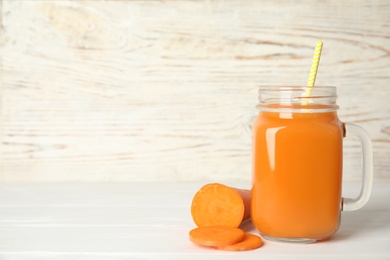 Photo of Freshly made carrot juice in mason jar on white wooden table. Space for text
