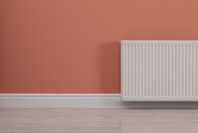 Photo of Modern radiator on color wall, space for text. Central heating system