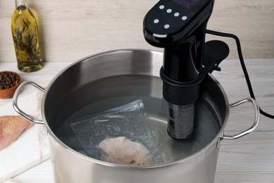Photo of Thermal immersion circulator and vacuum packed meat in pot on white wooden table. Sous vide cooking