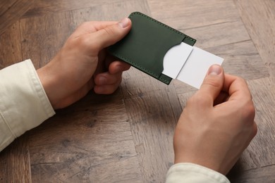 Photo of Man holding leather business card holder with cards at wooden table, closeup