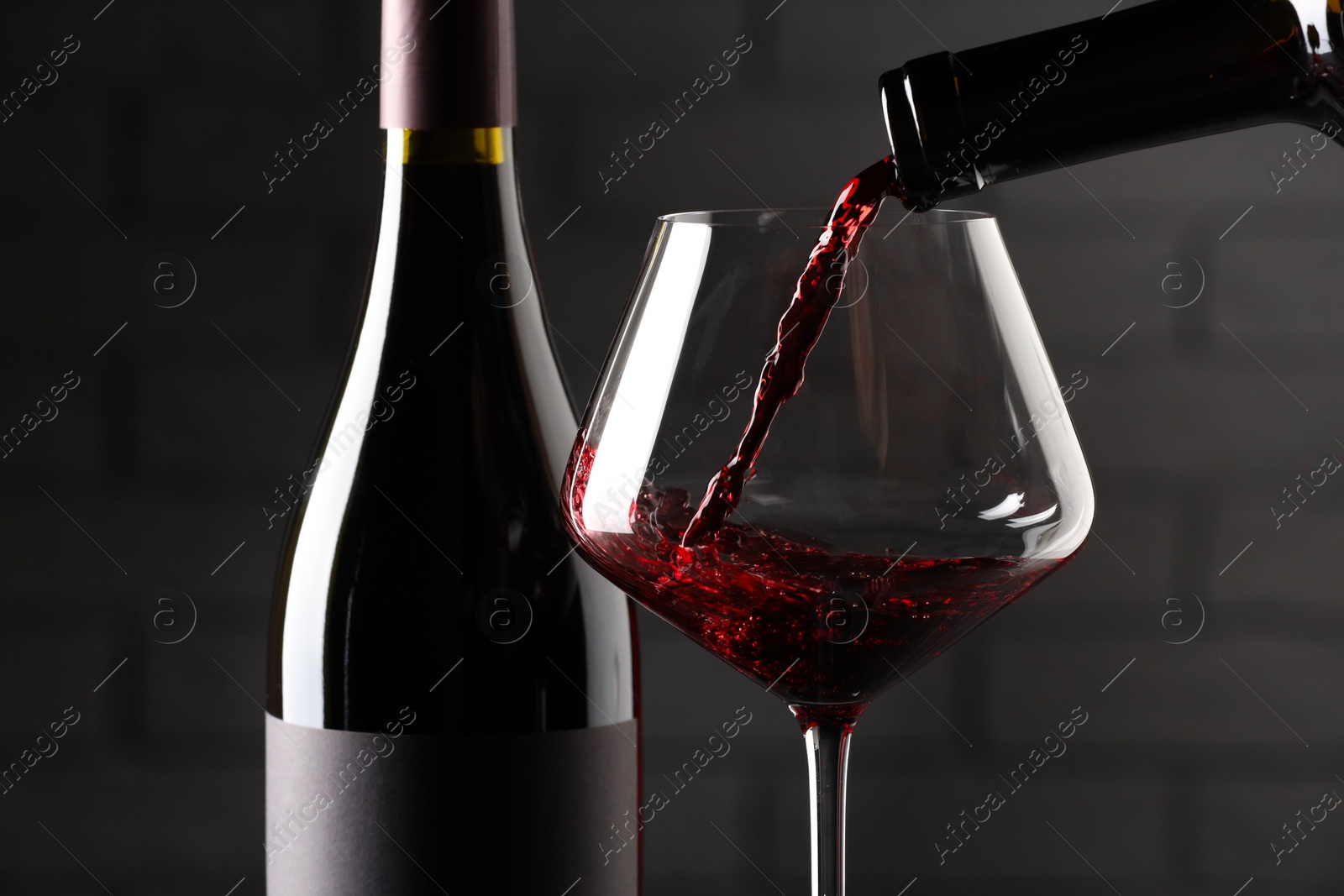 Photo of Pouring red wine into glass and bottles against brick wall background, closeup