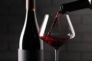 Photo of Pouring red wine into glass and bottles against brick wall background, closeup