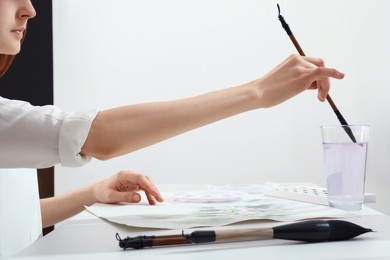 Photo of Woman wetting brush at white table indoors, closeup. Watercolor artwork